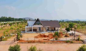 Modern house under construction in a rural yard, with a triangular glass front and piles of dirt and building materials nearby.